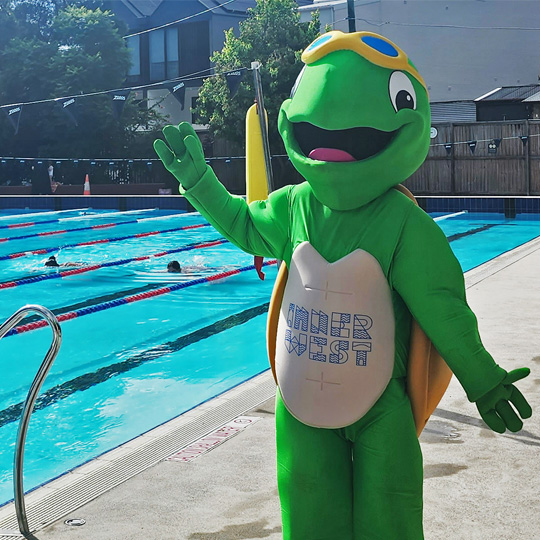 Terry the Turtle Aquatics mascot standing on the side of an outdoor pool waving